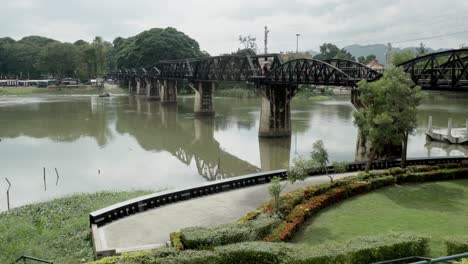 A-tilt-reveal-shot-of-the-iconic-Bridge-over-the-River-Kwai,-a-World-War-2-historical-landmark-and-a-popular-tourist-attraction-in-Kanchanaburi,-Thailand
