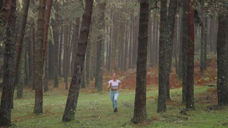 Female-athlete-running-through-natural-misty-forest-towards-camera,-slow-motion