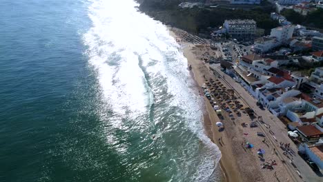 Aerial-shot-of-waves-crashing-at-beautiful-beach-in-front-of-a-little-fishing-village