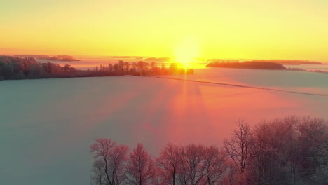 Golden-sunset-reflecting-off-the-snow-in-a-countryside-field-or-frozen-lake---aerial-sliding-flyover