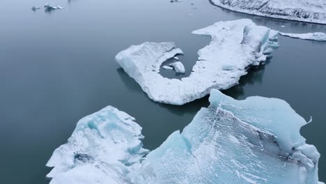 Aerial-birds-eye-shot-of-giant-icebergs-in-glacial-lake-during-bright-day-in-Iceland---Tilt-up-shot