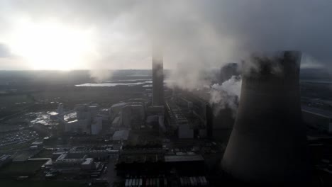 Aerial-view-of-UK-power-station-cooling-towers-flying-through-smoke-steam-emissions-at-sunrise