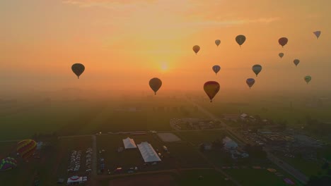 Eine-Luftaufnahme-Mehrerer-Heißluftballons,-Die-Während-Eines-Festivals-Mit-Zuschauern-An-Einem-Sommertag-In-Den-Frühen-Nebel-Mit-Einer-Roten-Sonne-Schweben