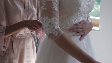 Mother-in-pastel-morning-robe-helps-her-daughter-put-on-wedding-dress,-slowmo