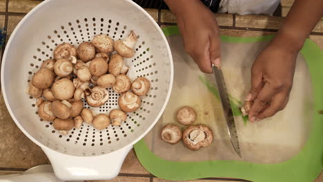 Cutting-the-stems-off-organic-cremini-mushrooms-to-prepare-them-for-a-homemade-soup-recipe---overhead-view-WILD-RICE-SERIES