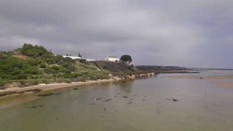 Volando-Bajo-Sobre-La-Tranquila-Playa-De-Cacela-Velha-Bajo-Un-Cielo-Nublado,-Barcos-De-Pesca-Anclados,-Portugal