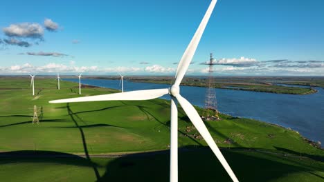 Wind-Turbine-spinning-generating-renewable-energy,-on-green-hills-along-river,-Montezuma-Hills,-California