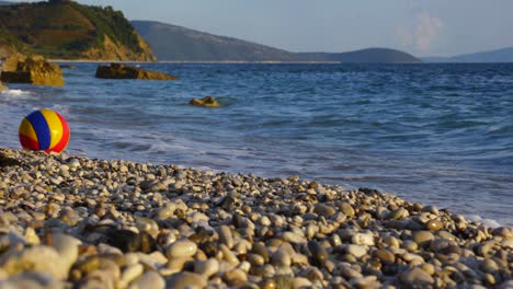 Beach-ball-floating-on-sea-waves-splashing-toward-pebbles-of-tranquil-beach-in-Mediterranean-coastline