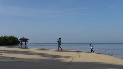 Niños-Locales-Jugando-En-La-Orilla-De-La-Playa-Con-Cielo-Azul-En-El-Fondo-En-Dos-Palmas-Island-Resort-And-Spa-En-Puerto-Princesa,-Palawan,-Filipinas