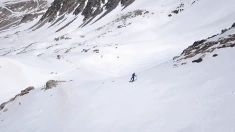 Aerial-view-of-a-man-climbing-up-a-mountain-on-skis-in-the-snow