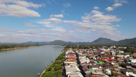 Aerial-footage-descending-and-revealing-the-rooftops-of-the-Walking-Street-then-the-Mekong-River-to-the-left-and-Laos,-Chiang-Khan,-Loei-in-Thailand