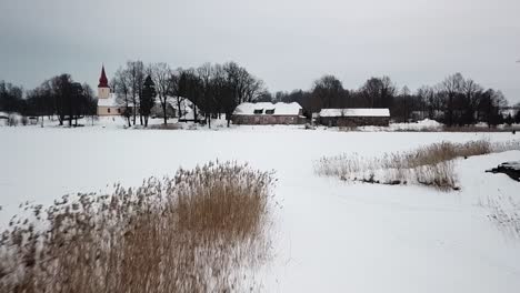 Dorfkirche-Und-Holzhäuser-Mit-Weißem-Schnee-Bedeckt,-Drohnenansicht-Aus-Niedrigem-Winkel