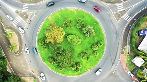 Top-down-aerial-zoom-out-view-of-a-traffic-roundabout-on-a-main-road-in-a-tropical-location
