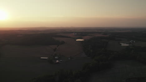 Wide-aerial-flyover-above-rural-farmland-at-evening-golden-hour