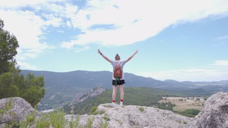 Young-woman-hiker-standing-on-a-mountain-cliff,raising-her-arms,Spain