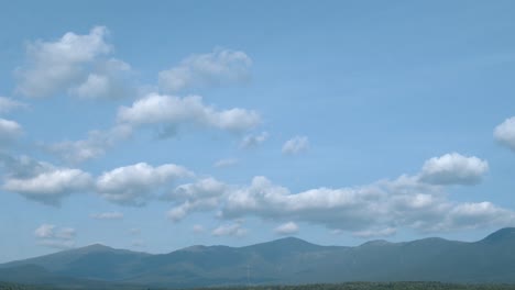 A-tilt-reveal-of-a-blue-cloudy-sky,-to-the-white-mountains-of-New-Hampshire,-to-a-green-forest-beyond-a-golf-course