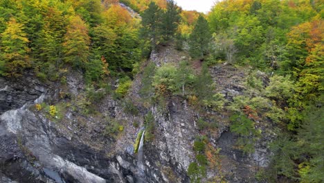 Wasser,-Das-Im-Herbst-Durch-Felsen-In-Einem-Schönen-Park-Mit-Bunten-Bäumen-In-Den-Alpen-Fällt
