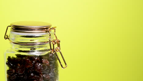 Detail-of-an-airtight-mason-jar-rotating-with-dehydrated-cranberry-on-a-neon-yellow-background
