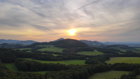 Aerial-view-of-hilly-landscape-of-meadows-woods-field-during-sunset-on-golden-sunset-background