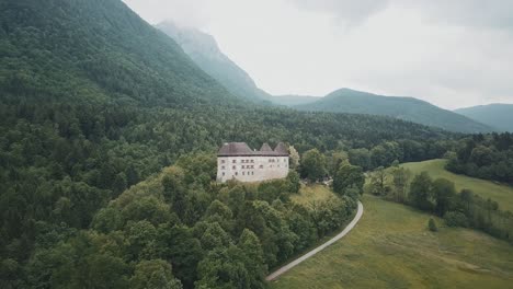 Drone-shot-of-a-german-palace-near-a-woodland-and-mountains-in-Pidingerau,-Upper-Bavaria,-Germany,-on-a-cloudy,-foggy-and-moody-day