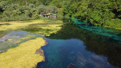 Drone-shot-of-the-Blue-Eye-in-Albania---drone-is-following-the-river-flow,-passing-a-restaurant-at-the-side