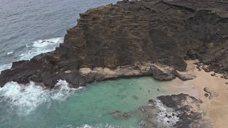 Aerial-view-of-beach-cove-with-swimmers-protected-by-rock-cliff
