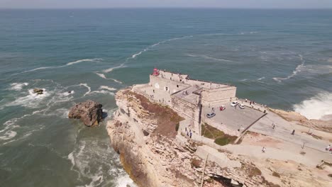 Aerial-flying-over-clifftop-Saint-Michael-the-Archangel-fort-and-Nazare-lighthouse-with-beautiful-seascape