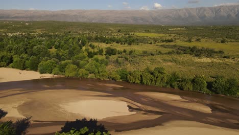 Dry-river-with-green-banks-and-mountains-in-background,-Cordoba,-Argentina