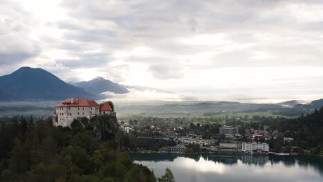 Aerial-View-Of-Bled-Castle-With-Lush-Forest-Along-Lake-Bled-And-City-In-Slovenia