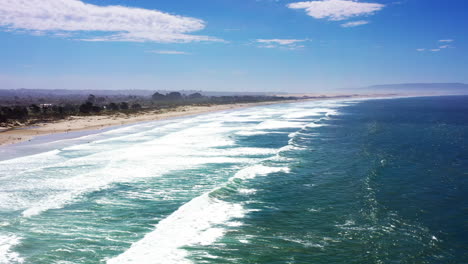 Aerial-view-of-Pismo-Beach,-California---panning-with-the-waves-as-the-roll-into-shore