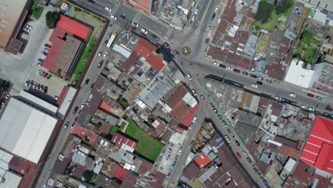 Drone-aerial-footage-of-traffic-cars,-trucks,-and-motorcycles-driving-through-the-urban-colonial-streets-of-Central-American-highlands-city-Quetzaltenango,-Xela,-Guatemala-in-Central-American