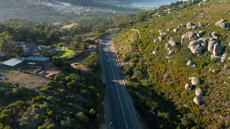 Cars-Driving-Through-Highway-In-The-Mountains-in-Llandudno-overlooking-Houtbay-in-Cape-Town,-South-Africa---aerial-shot