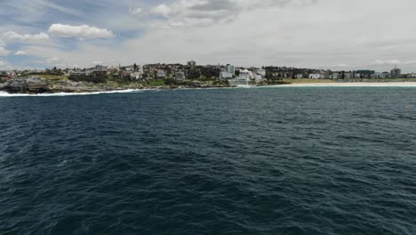 Drone-flying-over-blue-waters-of-Bondi-Beach,-New-South-Wales,-Sydney-in-Australia