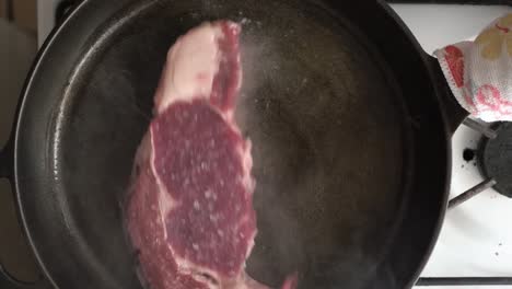 Placing-a-raw-steak-into-a-hot-cast-iron-skillet-with-oil---Overhead-view