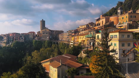 Wide-shot-showing-beautiful-old-buildings-of-Nevi-City-lighting-by-sunset-with-tower-in-background,Italy