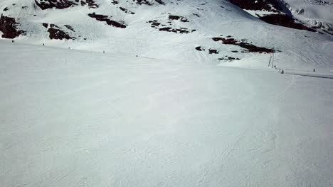 Drohnenaufnahme-Einer-Schneeebene-In-Den-Schweizer-Alpen-Mit-Menschen,-Die-Bergab-Skifahren-Und-Snowboarden