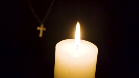 Kleine-Kerzenflamme-Brennt,-Während-Im-Hintergrund-Ein-Kleines-Silbernes-Kruzifix-Hängt