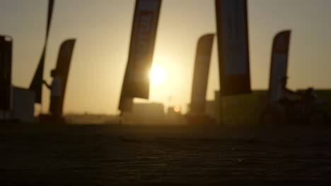 Dakar-Rally-motorcycle-riding-past-with-warming-golden-sunset-behind-flags