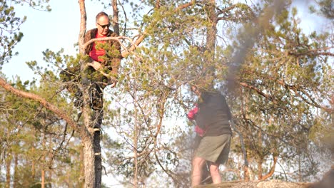 Multi-generation-family-hiking-on-mountain-hill-top,-grandmother-helping-granddaughter-get-up-into-a-lookout-tree-with-grandfather