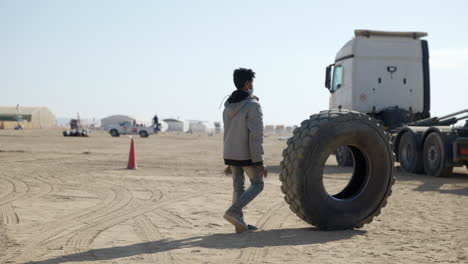 Hombre-árabe-Local-Recogiendo-Neumáticos-En-El-Rally-Dakar,-De-Izquierda-A-Derecha