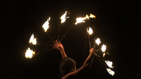 Asian-woman-spinning-brightly-lit-fire-fans-with-dark-background,-filmed-in-slow-motion-as-tight-close-up