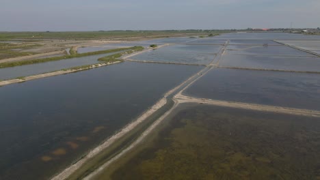 4K-Aerial-Drone-Footage-Flying-Low-Over-the-Salt-Flats-Filled-with-Water-and-Wildlife-in-Phetchaburi,-Thailand
