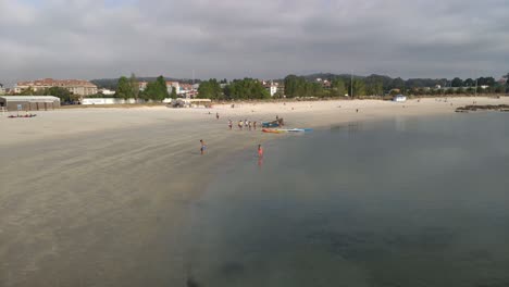 two-children-playing-soccer-and-a-group-of-teenagers-train-and-prepare-their-canoes-to-practice-rowing-on-a-cloudy-morning,-blocked-panoramic-shooting,-Porto-Novo,-Galicia,-Spain