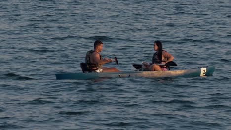 Couple-on-a-water-in-wooden-rowing-boat-during-sunset,-slow-motion