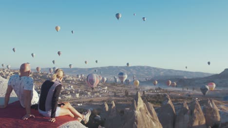 Paar-Sitzen-Zusammen-Und-Beobachten-Die-Heißluftballons-Kappadokien