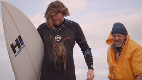 Marokkanischer-Fischer-Klebt-Oktopus-An-Die-Neoprenanzüge-Eines-Touristischen-Surfers,-Alle-Lächeln