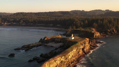 Oregon-Coast-Lighthouse-illuminated-by-setting-sun,-aerial-view