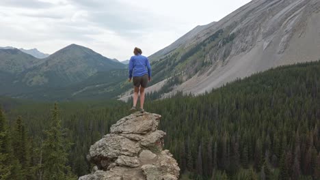 Hiker-stepping-on-ledge-admiring-mountain-view-approached-Rockies-Kananaskis-Alberta-Canada