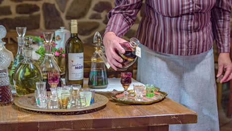 woman-pour-liquor-on-crystal-glasses,-table-with-spirits-bottles