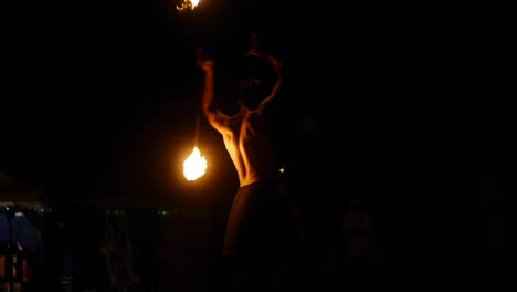 Asian-male-spinning-dual-ended-fire-stick-in-acrobatic-style-from-backside,-filmed-in-handheld-style-from-low-angle